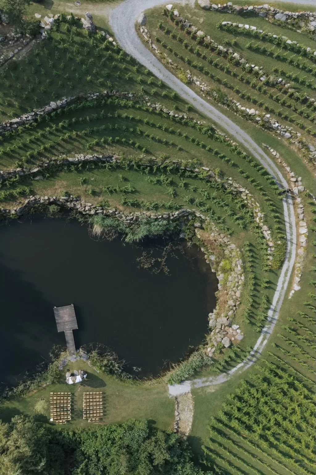 Aerial view of terraced vineyards and lakeside ceremony setup at Château Ste. Agnès, surrounded by lush greenery and curved stone paths.