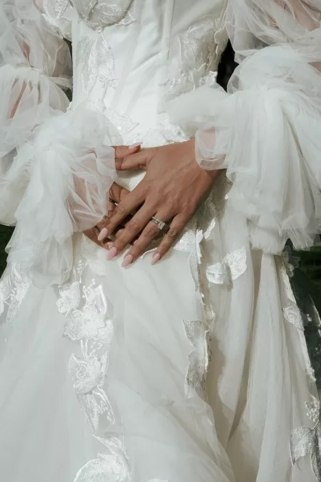 Close-up of the bride’s hands and engagement ring resting on a detailed lace wedding gown with delicate tulle sleeves at Common Goods.