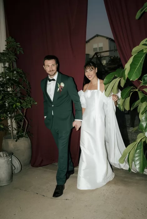 Bride and groom entering through deep red curtains at Common Goods, holding hands and smiling during their reception entrance.