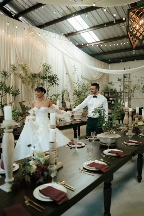 Bride and groom entering a styled reception dining space with long tables, candles, and draped fabric ceiling at Common Goods.