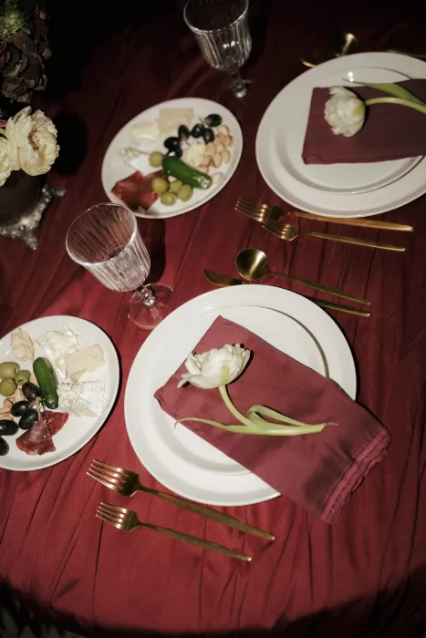 Burgundy reception table setting at Common Goods with gold cutlery, crystal glassware, and tulips placed on folded napkins.
