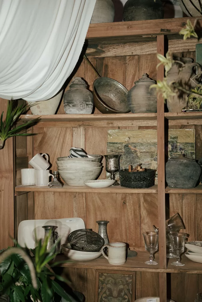 Rustic wooden shelves filled with vintage pottery, glassware, and décor inside Common Goods wedding venue.