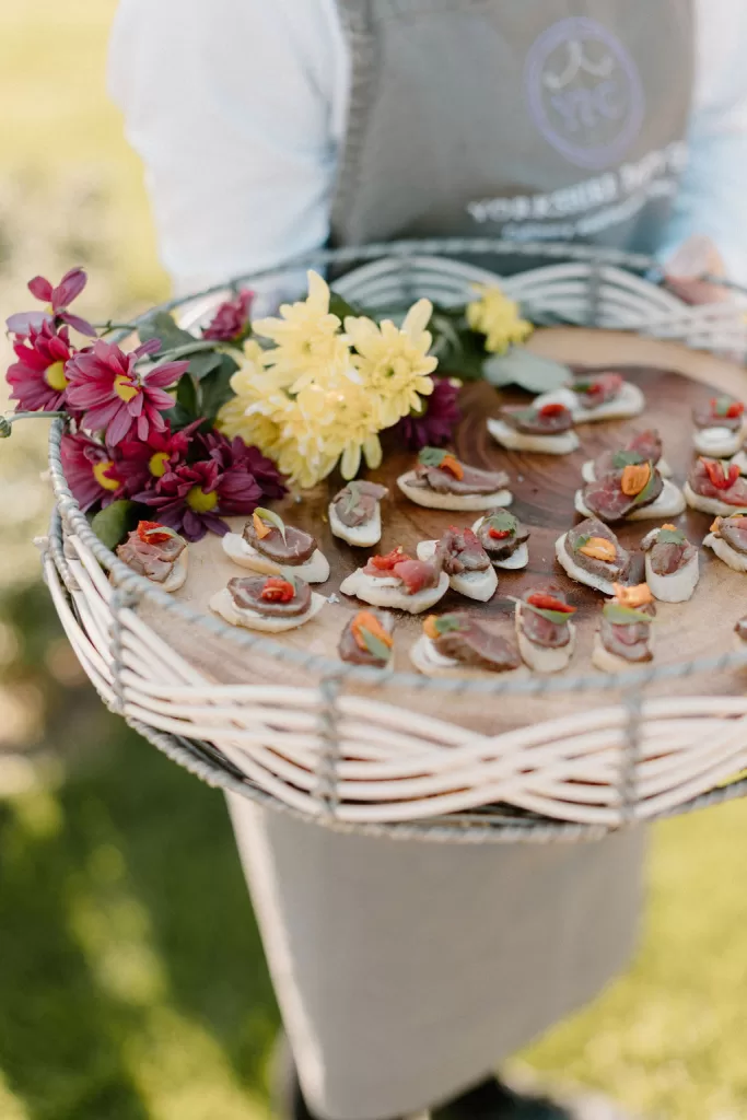 Waiter serving gourmet wedding canapés on tray with colourful florals at Hotham Hall Estate