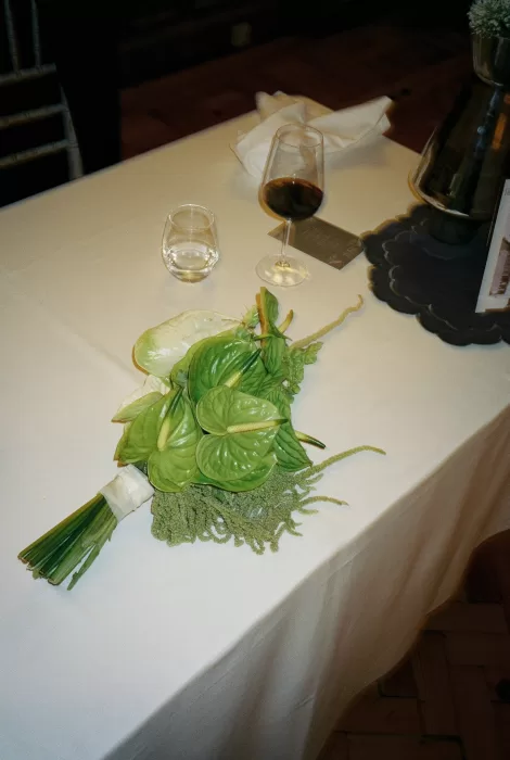 Modern green bridal bouquet resting on a reception table with wine glasses during the wedding at Infante Sagres.