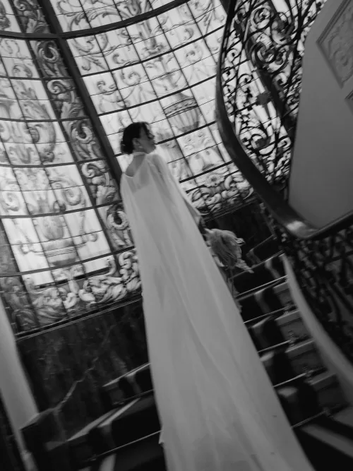Bride walking past the stained glass staircase inside Infante Sagres, her long cape trailing behind.