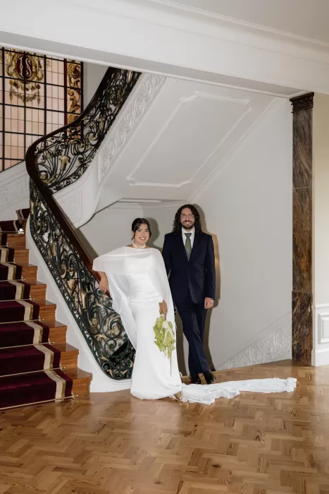Bride and groom posing together beside the sweeping staircase inside the historic Infante Sagres hotel.