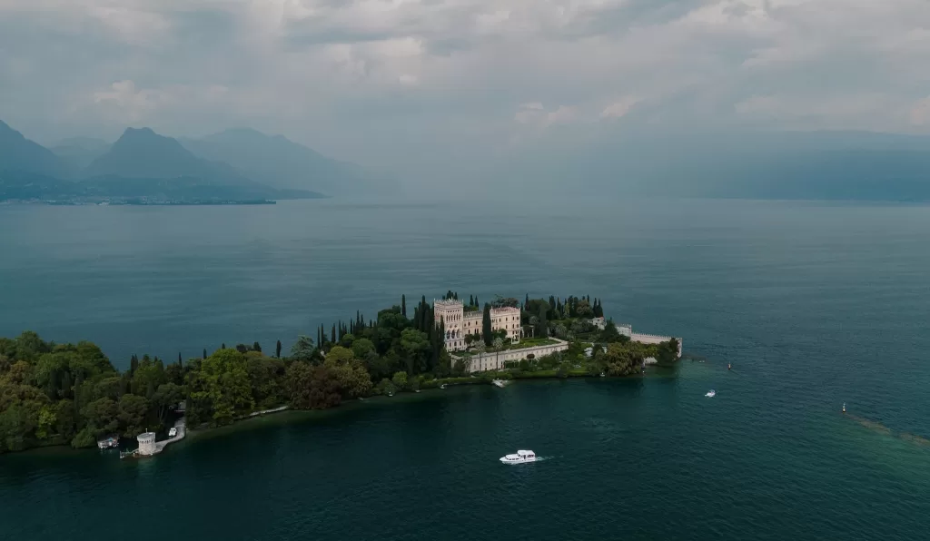 Aerial view of Isola del Garda surrounded by deep blue lake and dramatic sky