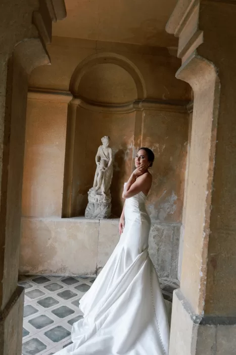 Bride posing beside classical statue in warm-toned interior at Isola del Garda