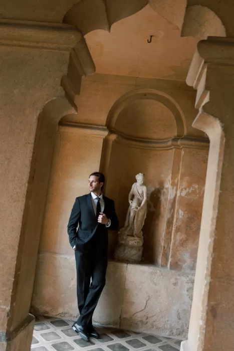 Groom portrait beside classical statue in warm-toned interior at Isola del Garda