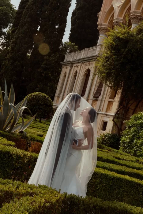 Couple embracing beneath veil in sculpted gardens with villa backdrop at Isola del Garda