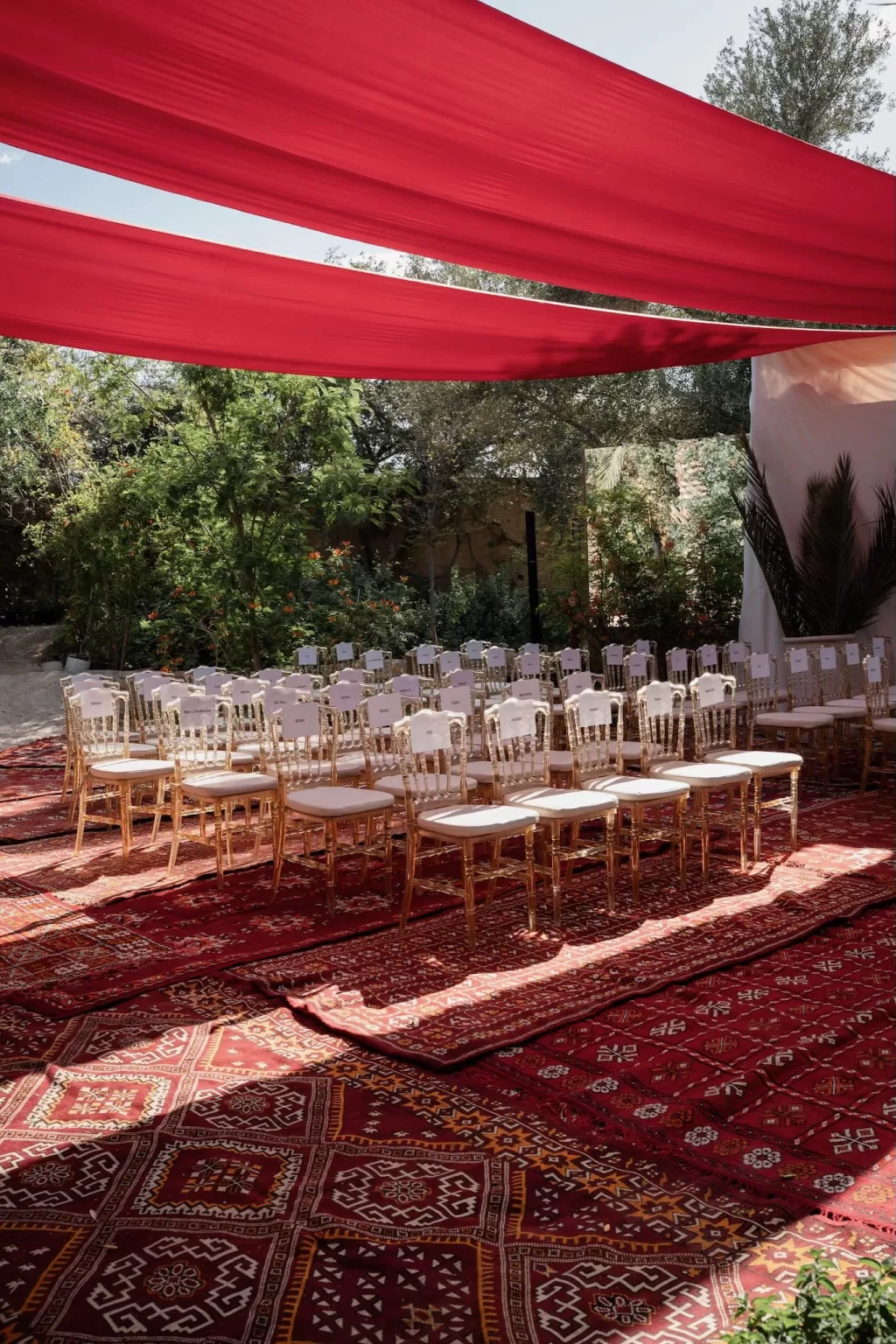 Rows of gold chairs arranged on layered Moroccan rugs beneath red canopy fabric at Jnane Tamsna.