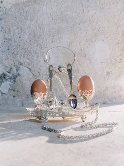 Antique silver egg cups with brown eggs and vintage spoons styled on stone at Mas de Chabran.