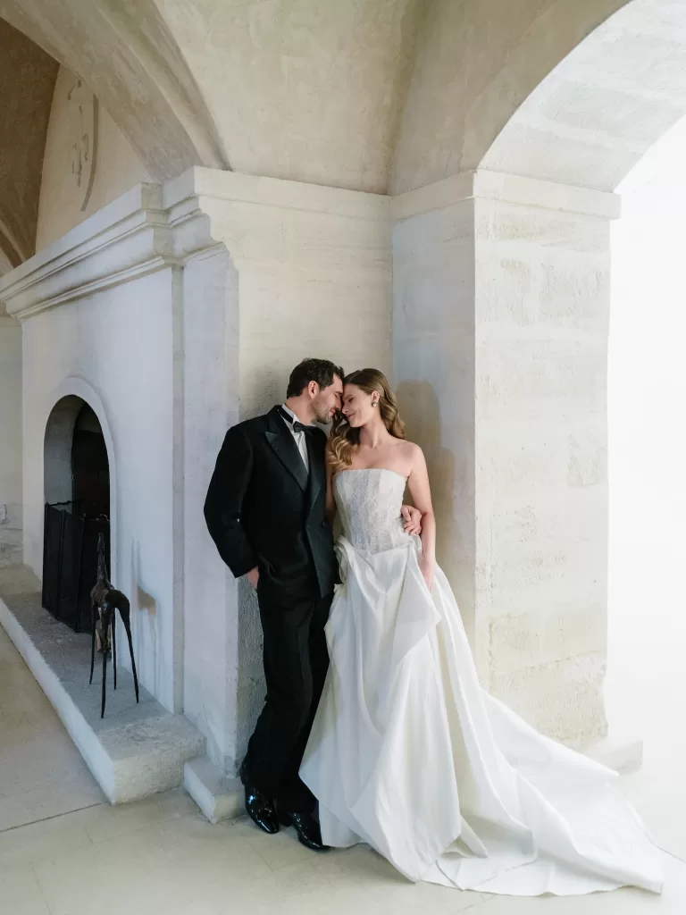 Bride and groom in black tie leaning together beneath a stone archway at Mas de Chabran.