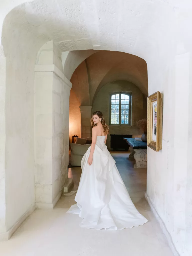 Bride in sculptural wedding gown standing in a vaulted stone hallway inside Mas de Chabran.