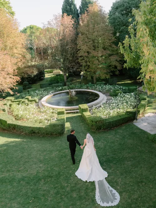 Bride and groom walking hand in hand toward the circular garden fountain at Mas de Chabran.
