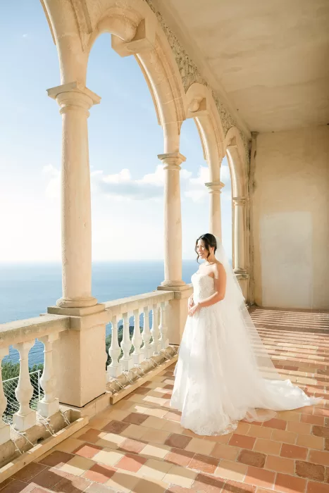 Bride standing on a sunlit terrace at Son Marroig with sweeping sea views and historic arches