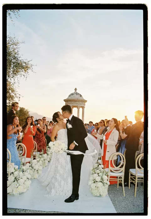 Bride and groom kissing in the aisle surrounded by guests and white florals at Son Marroig