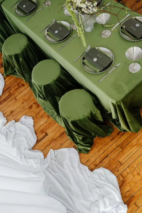 Reception table with green velvet linens, matching stools and modern place settings on wooden floors at Studio Sunset Chicago