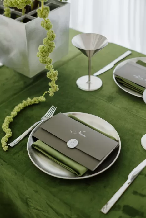 Minimal place setting with green napkin, wax seal menu and metallic tableware at Studio Sunset Chicago