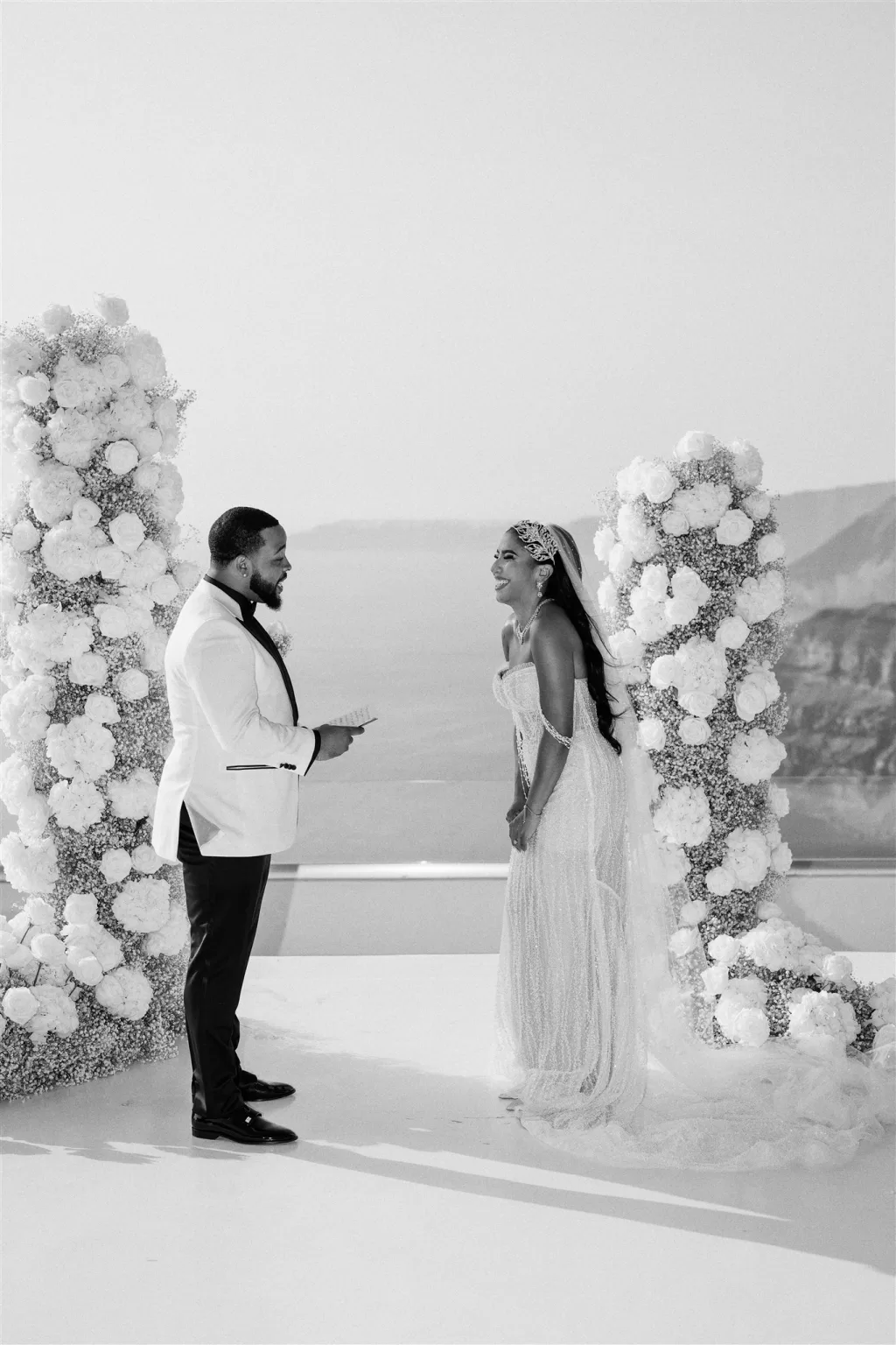 Black and white moment of couple laughing during vows framed by floral installations