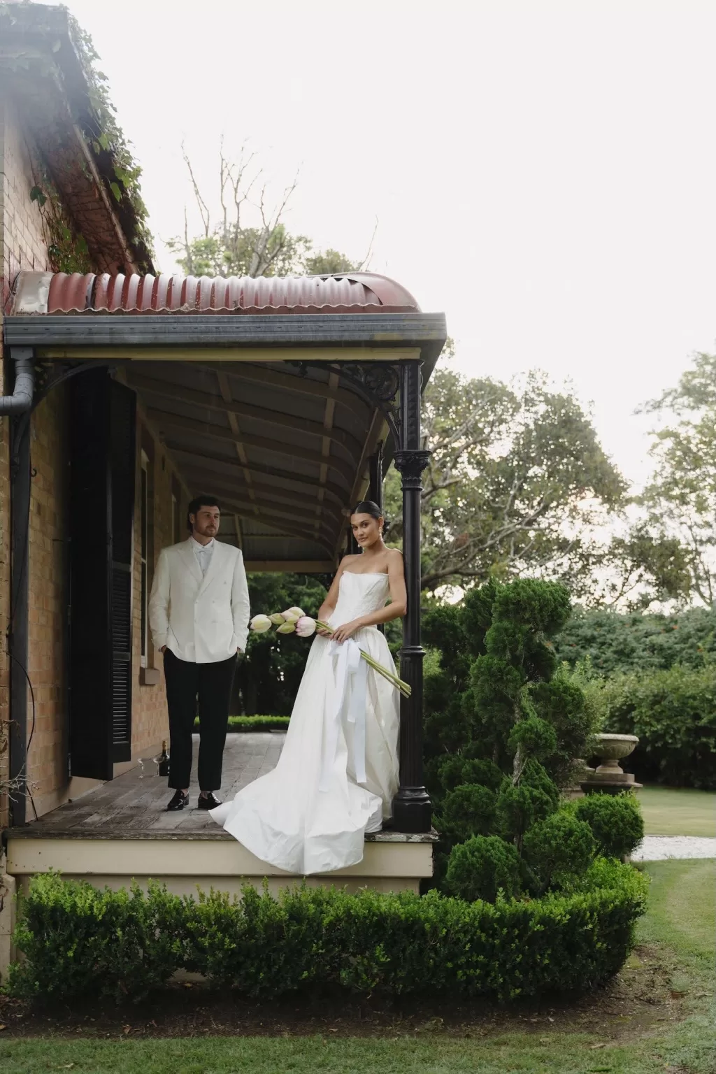Bride holding lotus bouquet while standing on the veranda with groom at Wallalong House.