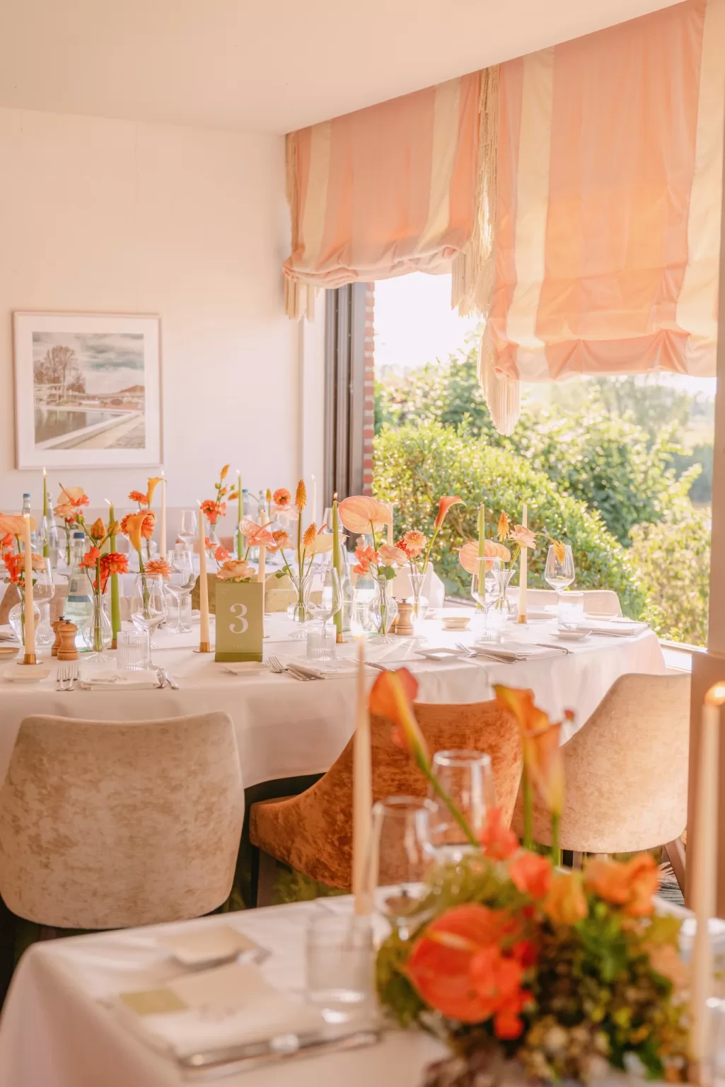 Sunlit reception table with orange florals and soft draping by Anne De Geyter Fotografie