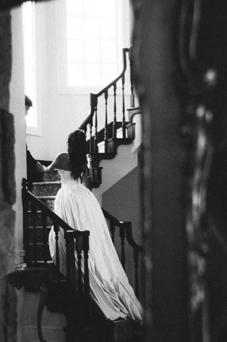 Black and white image of the bride moving up the staircase in her full gown.