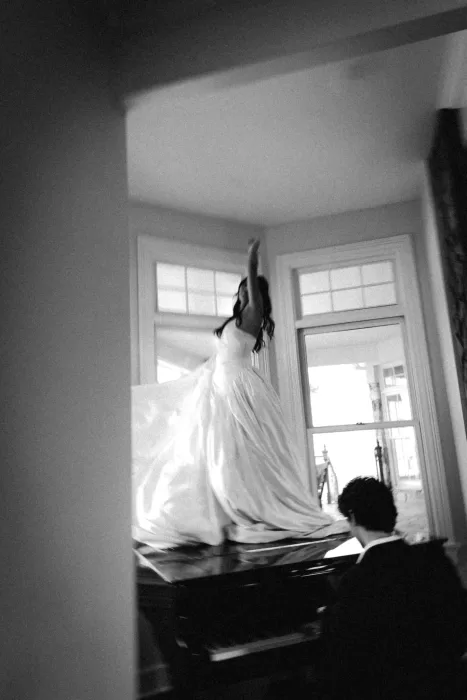 Soft black and white image of the bride moving across a grand piano.