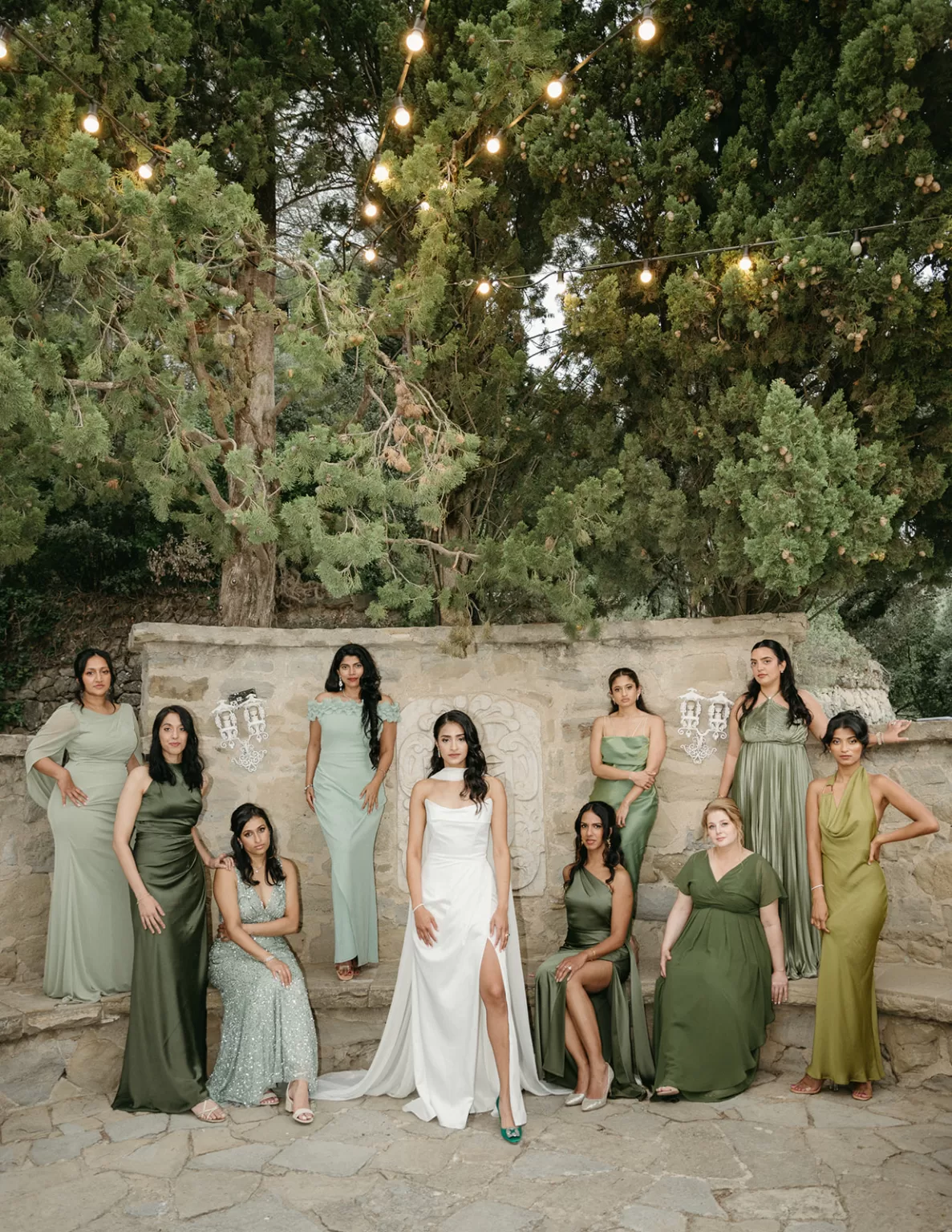 Bridesmaids in tonal green dresses gathered in a stone garden setting