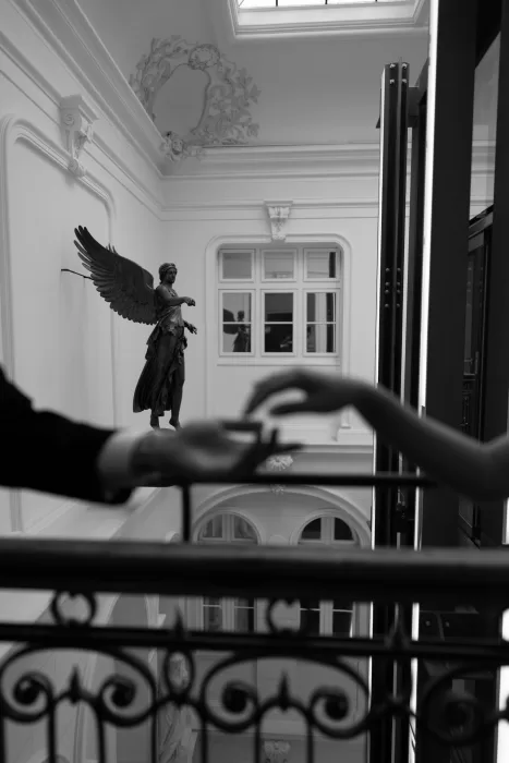 Minimalist composition of bride and groom reaching toward each other with a classical statue in the background