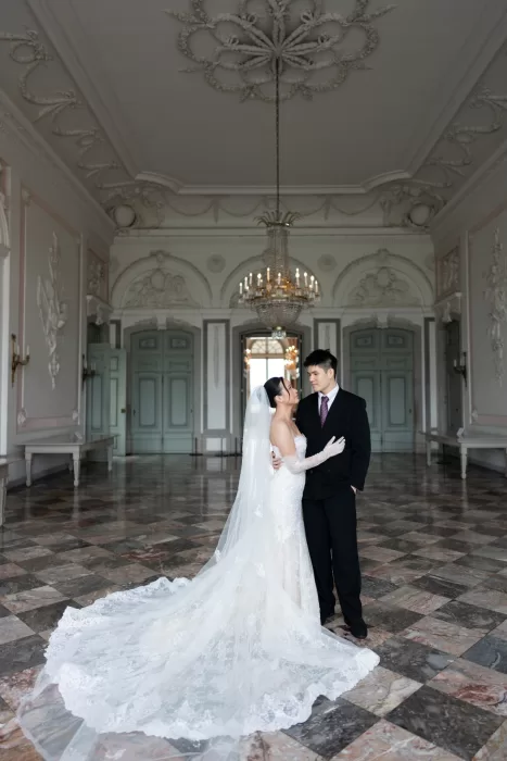 Bride and groom embracing beneath a chandelier in a grand ballroom with marble floors