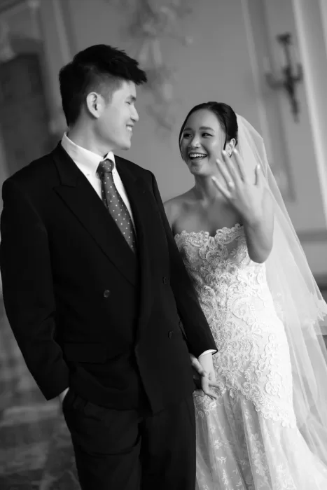 Bride laughing and showing her ring while walking with groom in a softly lit elegant interior