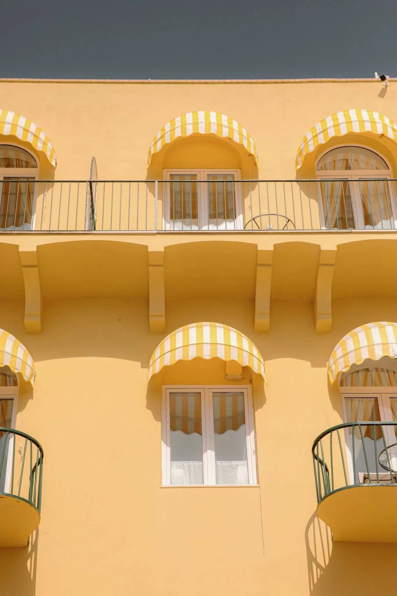 Iconic yellow-striped awnings and balconies of Caesar Augustus Capri glowing under the Mediterranean sun.