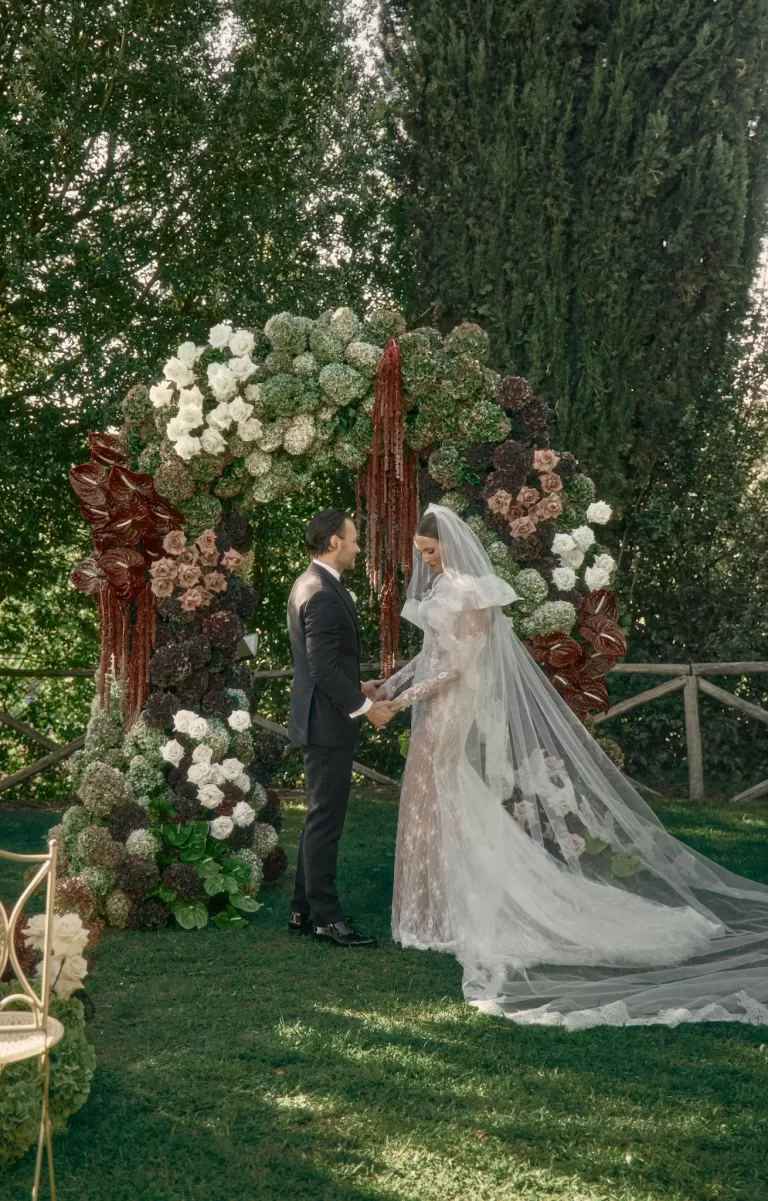 Bride and groom standing beneath dramatic floral ceremony arch