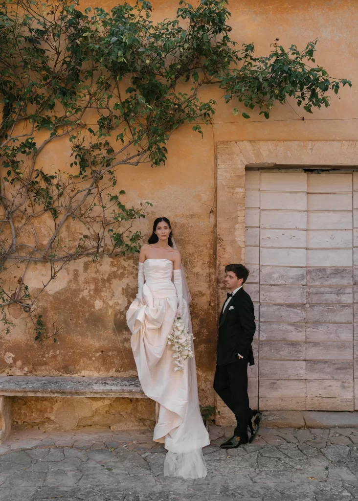 Bride and groom posing against warm textured wall with greenery in romantic Italian setting