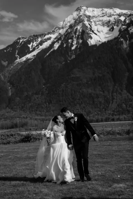 Black and white photo of bride and groom walking together with mountain backdrop at Fraser River Lodge