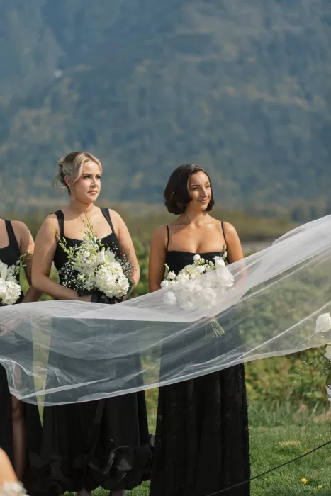 Bridesmaids in black dresses holding white bouquets during outdoor ceremony at Fraser River Lodge