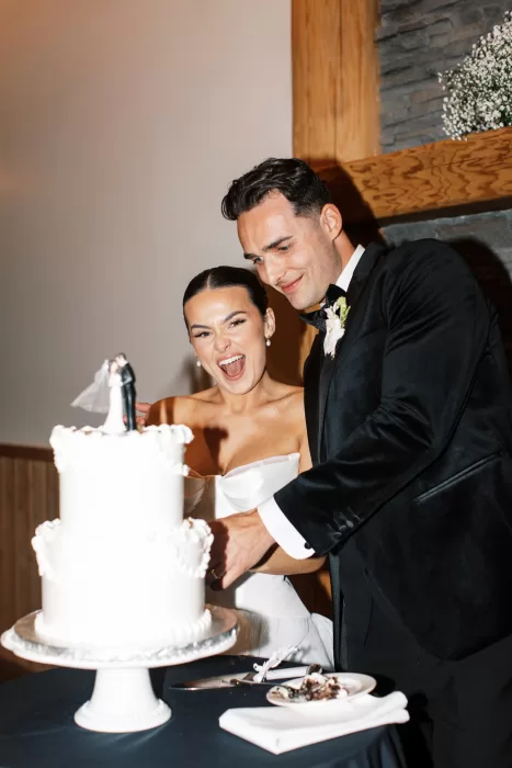 Bride and groom cutting wedding cake indoors at Fraser River Lodge, smiling during reception