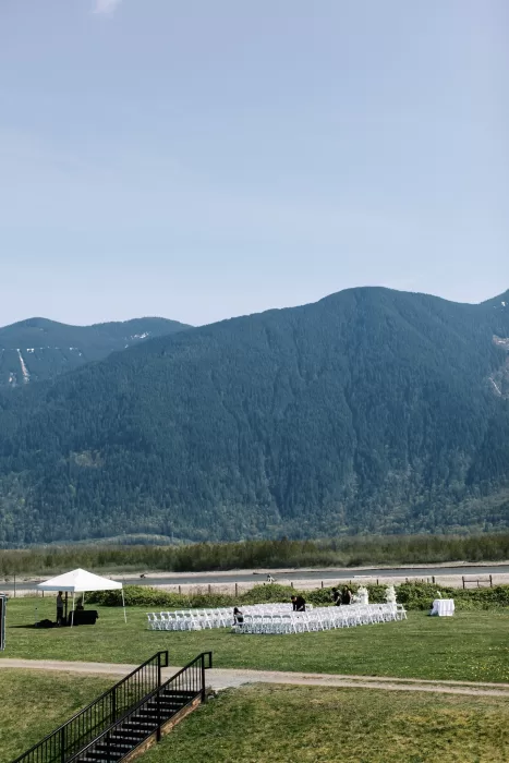 Wide view of outdoor ceremony setup with chairs and mountains behind Fraser River Lodge