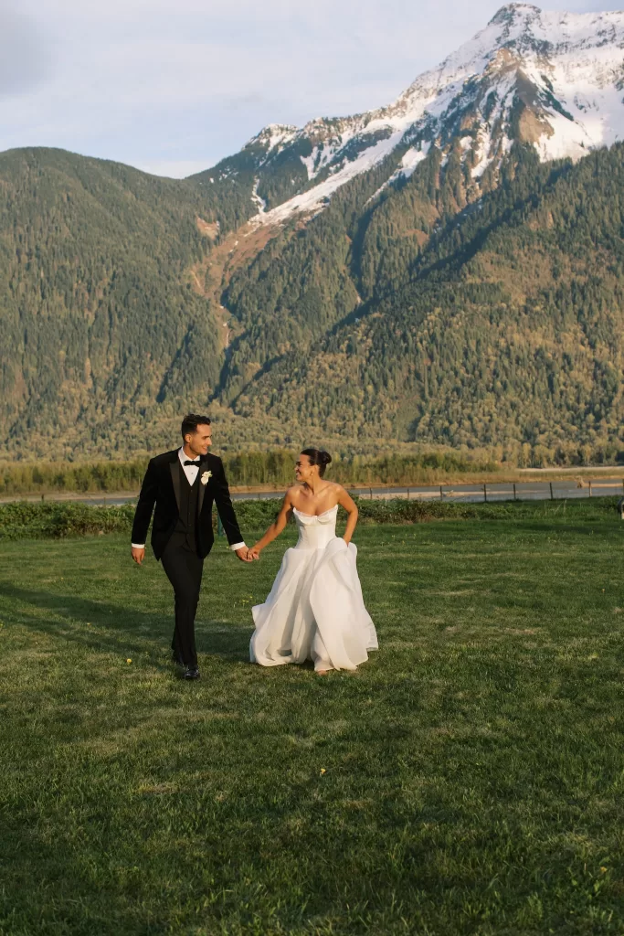 Bride and groom walking across lawn with veil flowing outside Fraser River Lodge