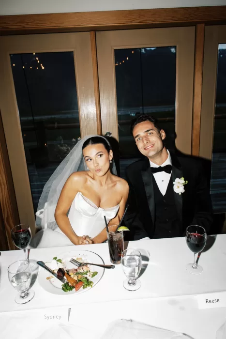 Bride and groom seated at reception table with drinks and dinner plates at Fraser River Lodge