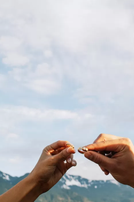 Couple holding wedding rings against mountain backdrop at Fraser River Lodge