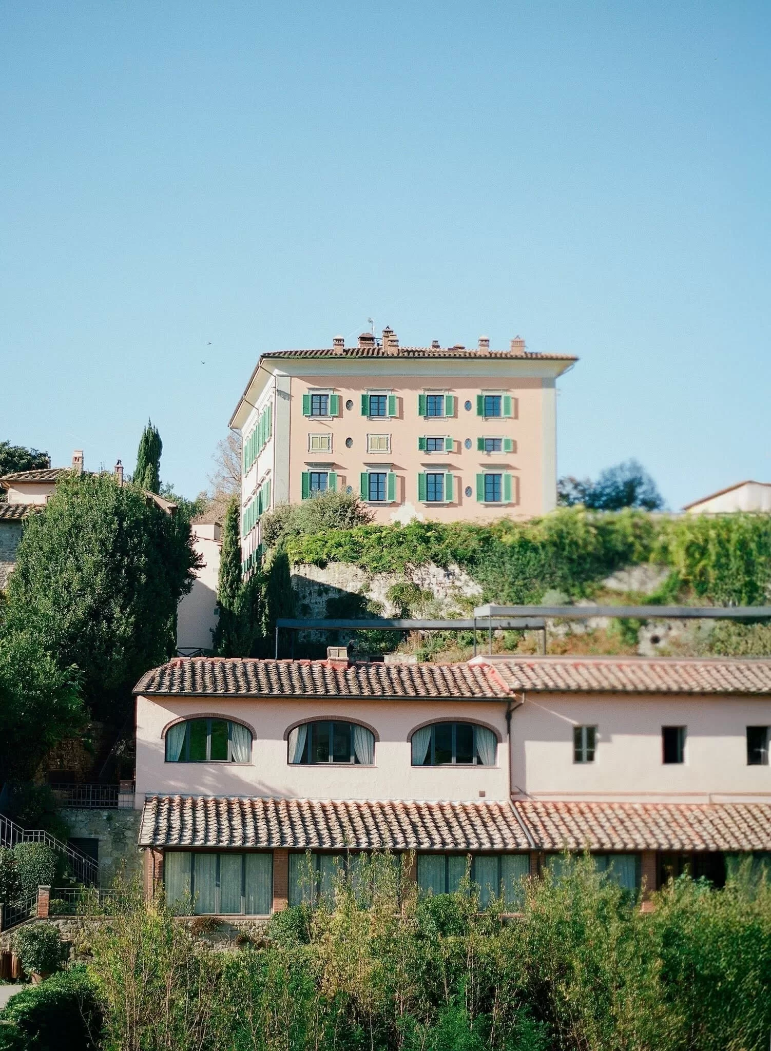 View of Il Borro’s pastel villa with green shutters nestled among Tuscan hills and cypress trees.