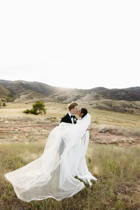 Couple kissing in the meadow with the bride’s veil moving in the wind at The Manor House.