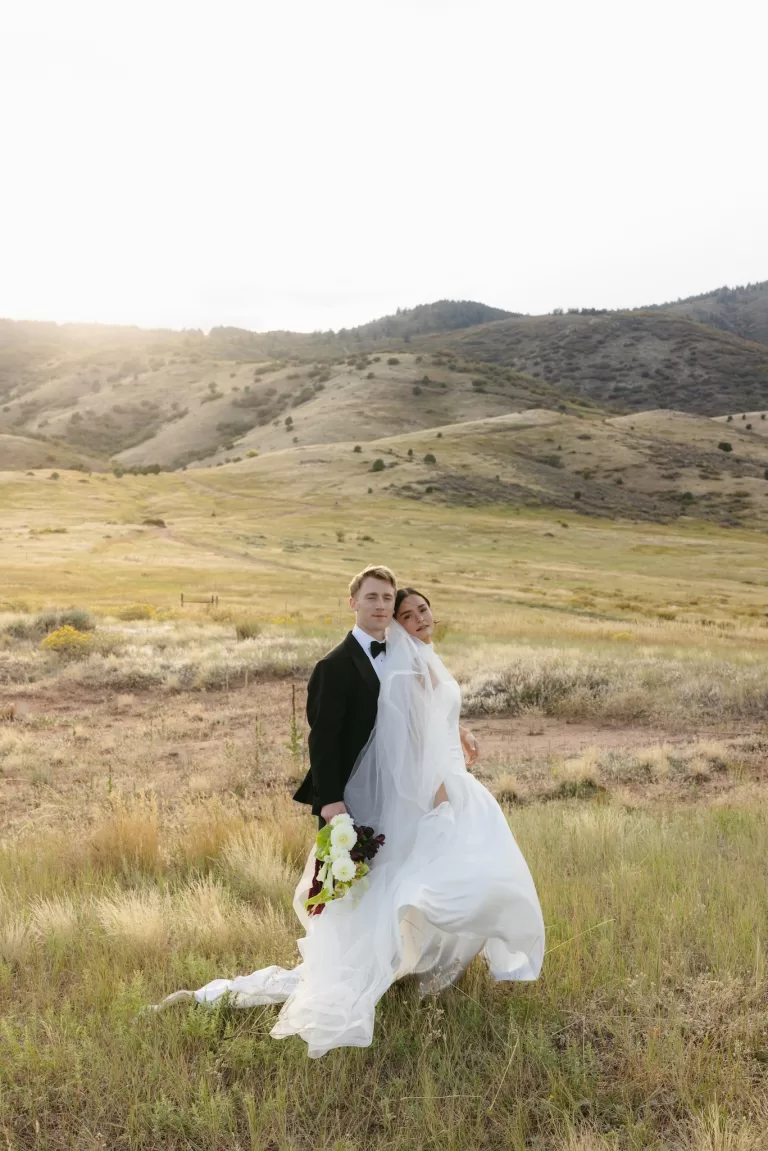 Newlyweds posing in the field at golden hour beside The Manor House in Colorado.