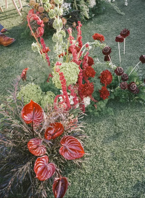 Bold red and green ceremony florals arranged along the aisle at Monserate Winery