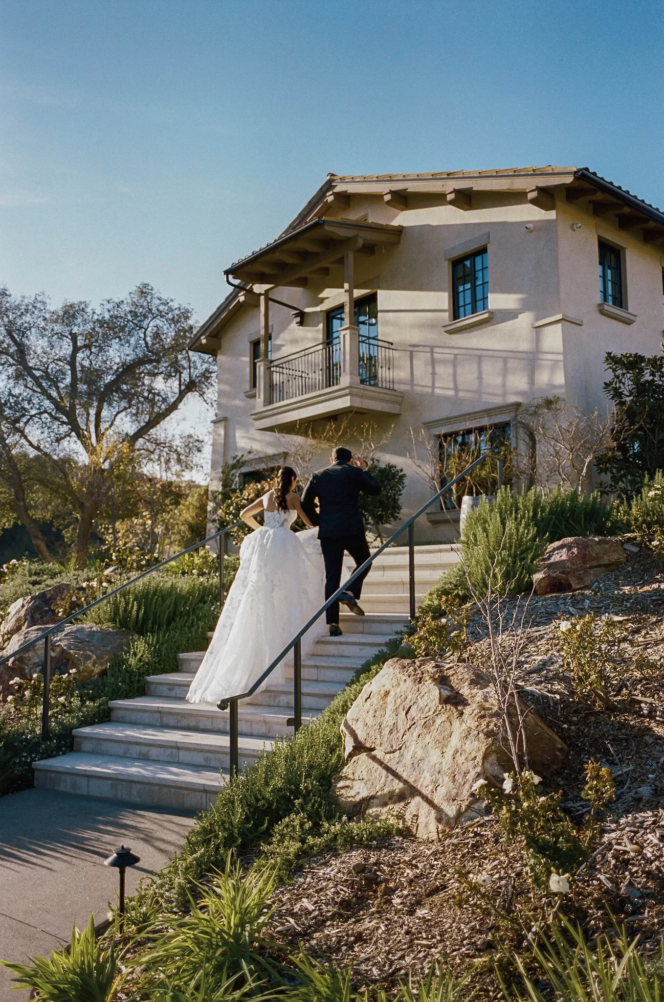 Couple walk up stone steps toward the warm stucco exterior of Monserate Winery