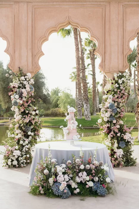 Wedding cake framed by abundant floral arrangements beneath arched pavilion at Palais Namaskar