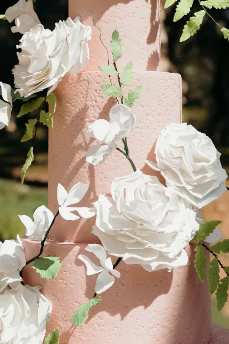 Close-up of elegant pink wedding cake adorned with white sugar flowers at Palais Namaskar