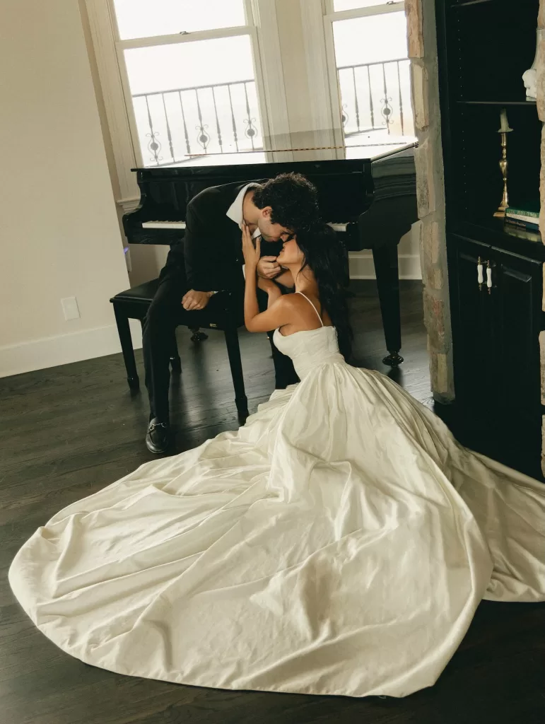 The couple pose beside a grand piano at Stone Haven, her gown spilling across the floor.